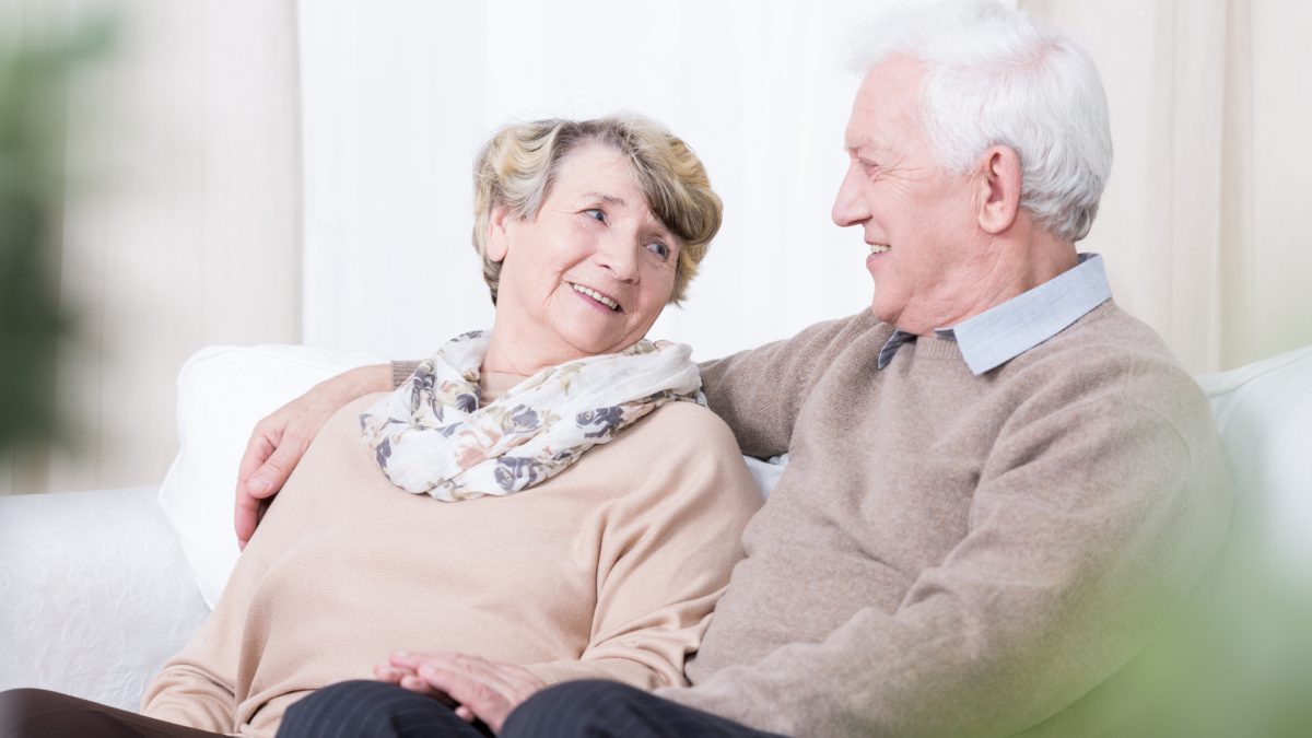 Elderly couple smiling and sitting together.